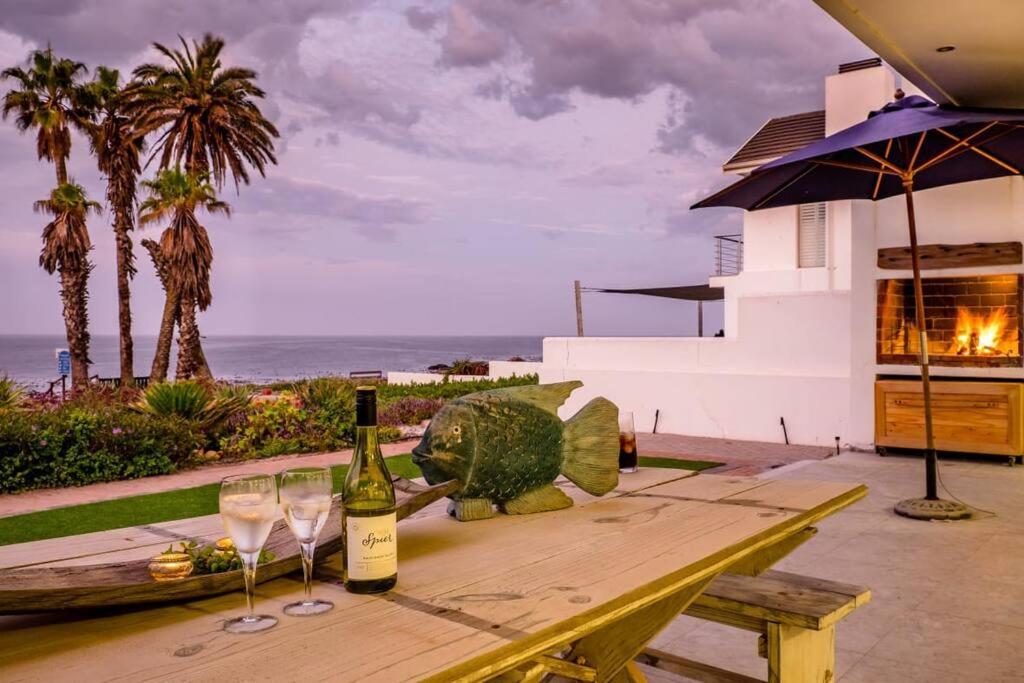 a wooden table with two wine glasses on it at Driftwood Beachfront Manor - Shelley Point in St Helena Bay