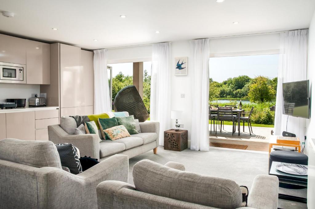 a living room with couches and a kitchen with a table at Luxury apartment with spa access on a nature reserve Dragonfly HM106 in Somerford Keynes