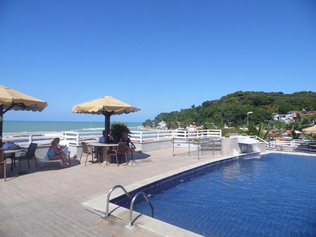 a swimming pool with tables and umbrellas next to the ocean at Sonia Flats Pipa's Bay - Flat 121 in Pipa