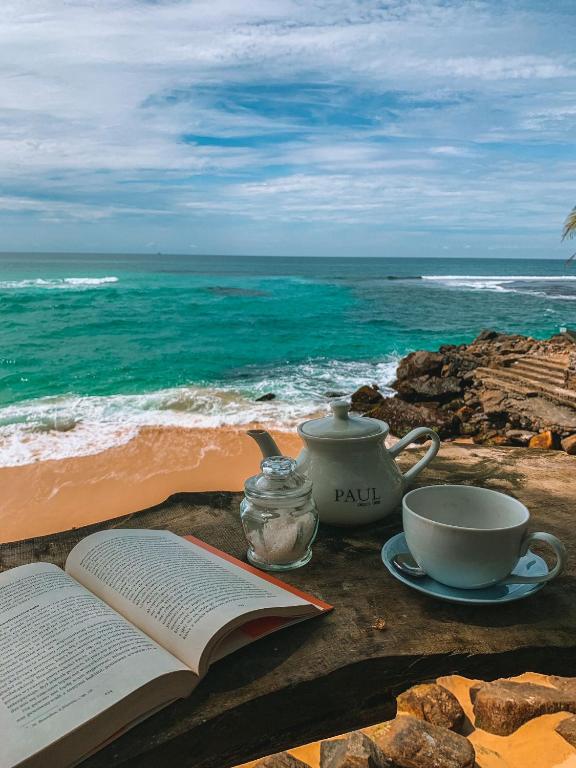 an open book and a cup of coffee on a table near the ocean at fantasea villa in Unawatuna