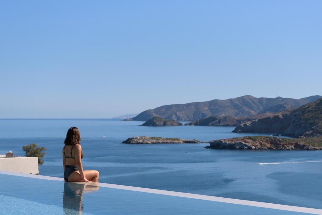 バリにあるNandana Luxury Villa, an infinite blue experience, By ThinkVillaの海を見下ろすスイミングプールの端に座る女性