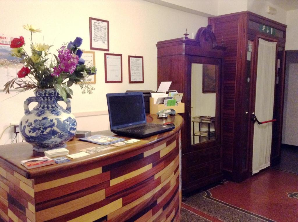 einen Schreibtisch mit einem Laptop und eine Vase mit Blumen darauf in der Unterkunft Hotel Bernheof in Genua