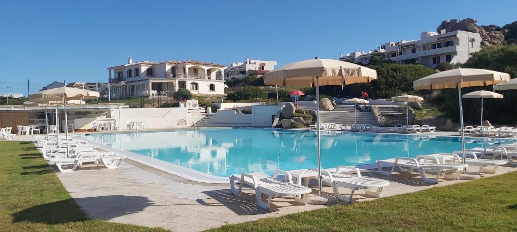 une grande piscine avec des chaises et des parasols blancs dans l'établissement Residence Baia Santa Reparata, à Santa Teresa Gallura