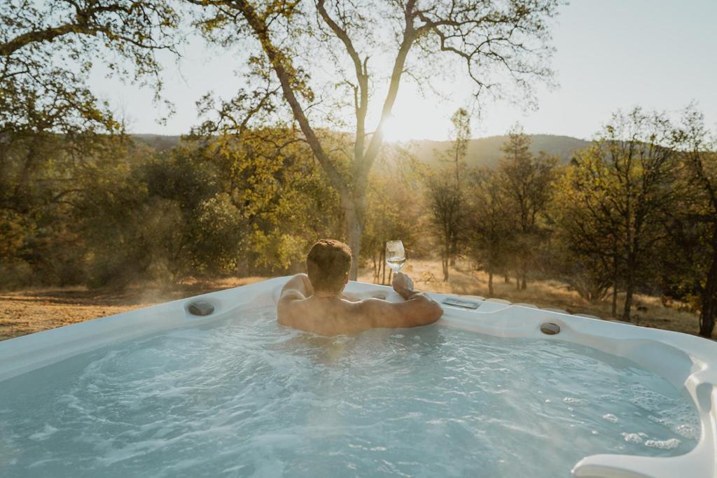 a man in a hot tub with a glass of wine at Glamour Mountain Getaway by Casa Oso with views and spa in Oakhurst