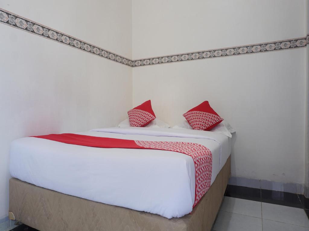 1 dormitorio con cama blanca y almohadas rojas en OYO 91900 Wisma Amrach, en Watampone