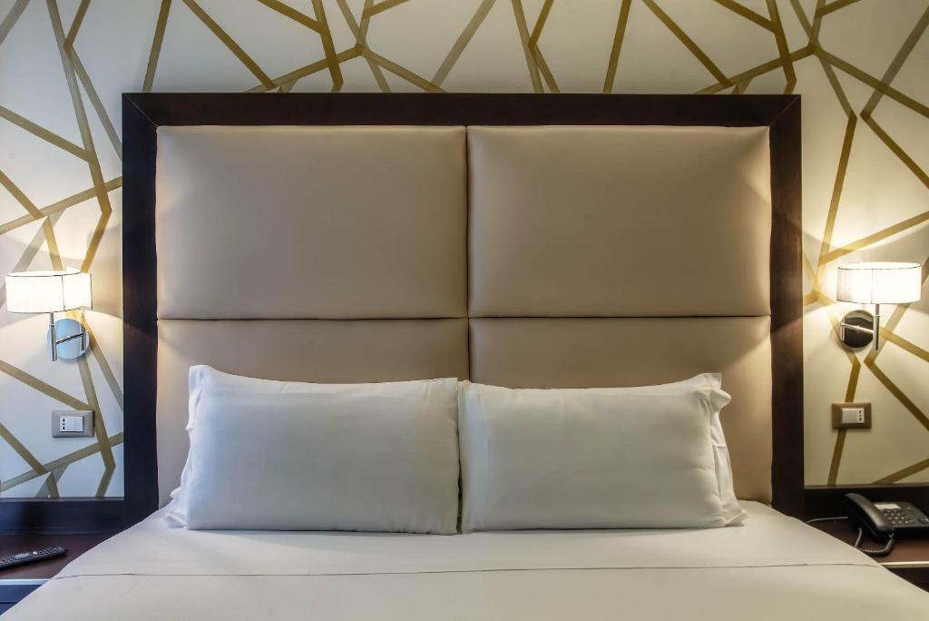 a bed with a headboard with two pillows and a phone at Catone District Hotel in Rome
