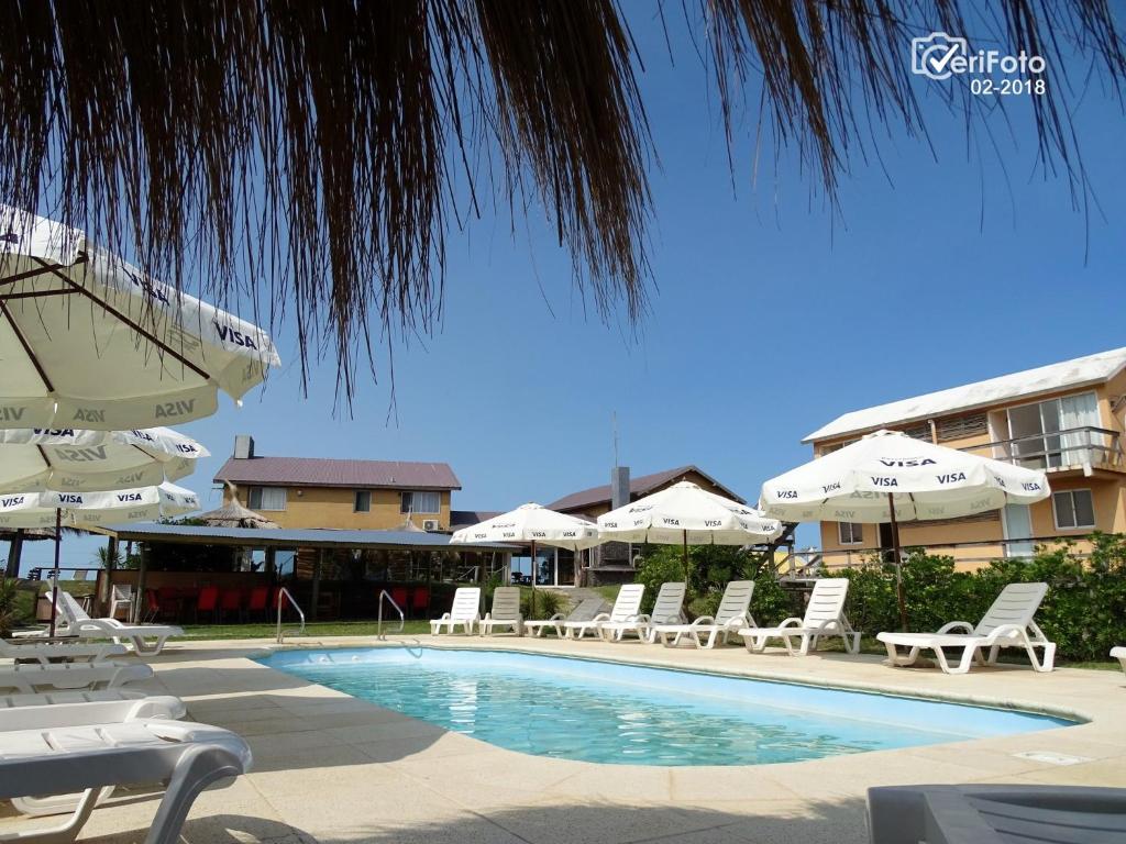 a swimming pool with white chairs and umbrellas at Hotel Aquarella in Punta Del Diablo