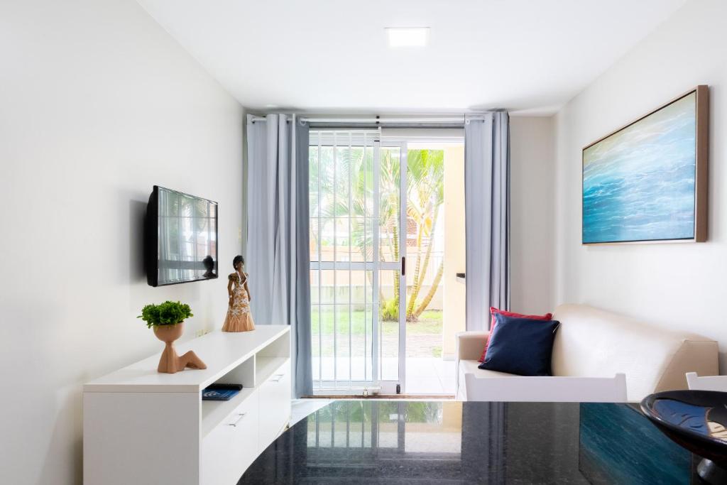 Il comprend un salon doté d'un mobilier blanc et d'une porte coulissante en verre. dans l'établissement Ocean Residence, à Porto de Galinhas