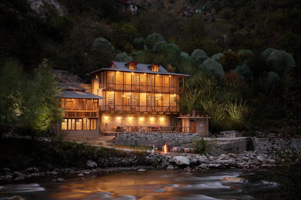 une maison éclairée la nuit à côté d'une rivière dans l'établissement Living Good - A Himalayan Boutique Stay, à Gushaini