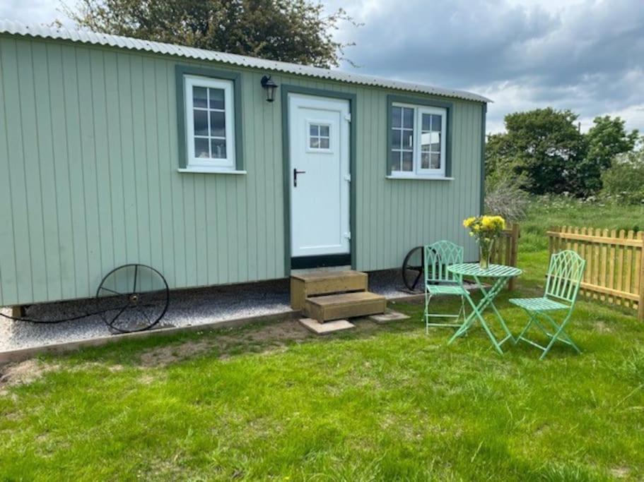 une maison verte avec une table et des chaises dans l'herbe dans l'établissement Shepherd Hut, à Warwick