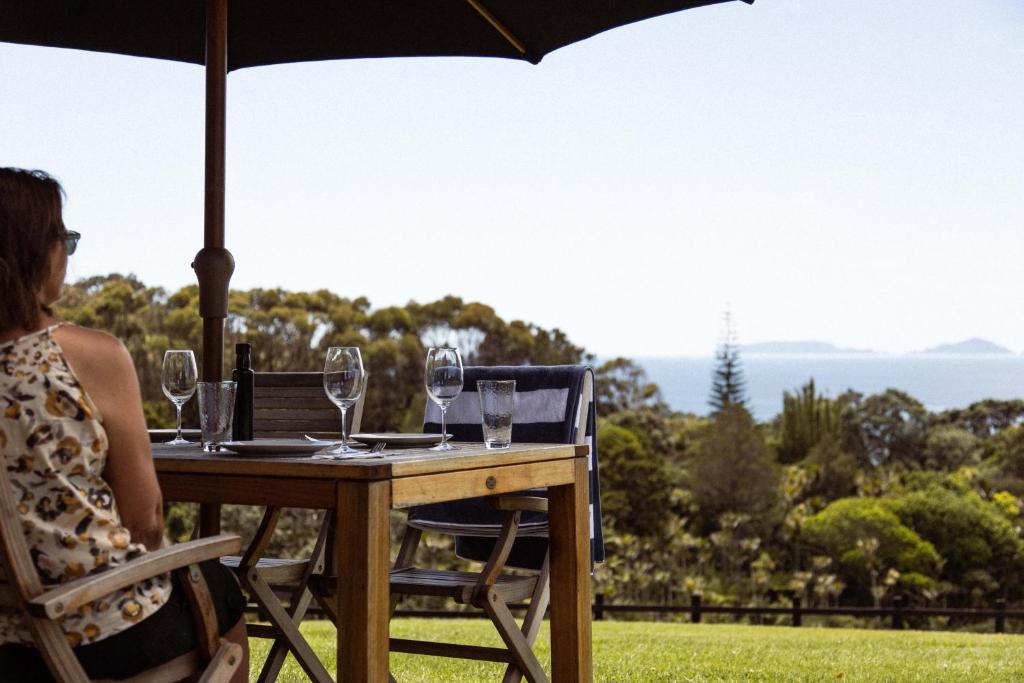 a woman sitting at a table with an umbrella at Vineyard Apartment in Tutukaka