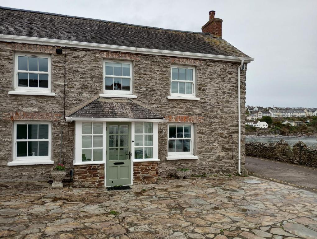 Casa de ladrillo con ventanas blancas y puerta verde en Quayside, en Porthscatho