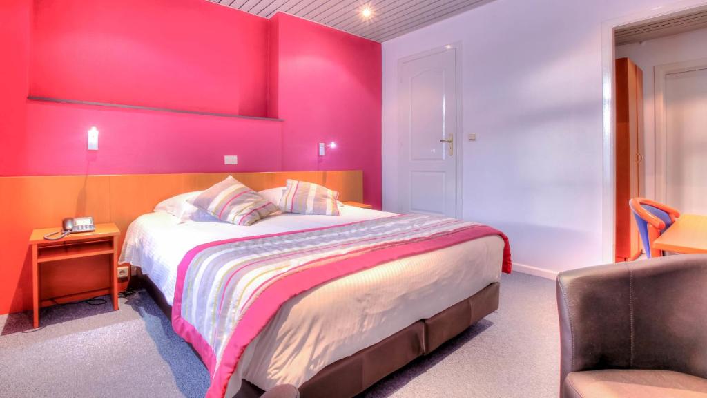 a pink bedroom with a bed and a chair at Hotel Le Terminus in Mons