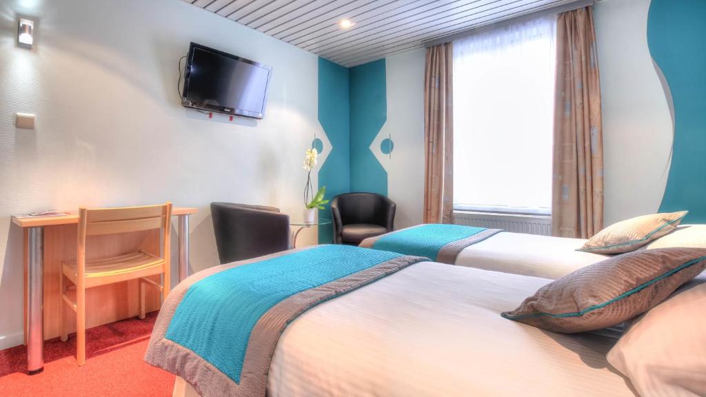 a hotel room with two beds and a desk and a television at Hotel Le Terminus in Mons