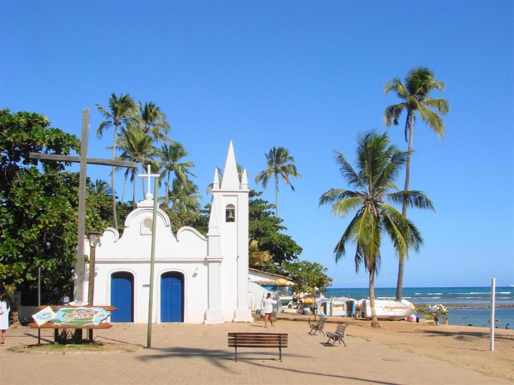 a white church on the beach with palm trees at Refugio Villa Verona Praia do Forte in Mata de Sao Joao