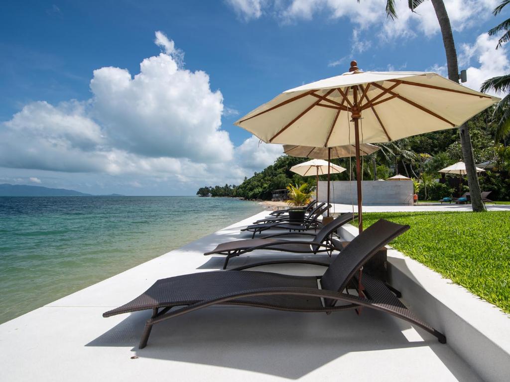 una fila de sillas y una sombrilla en la playa en Villa Chi Samui - SHA Extra Plus, en Mae Nam
