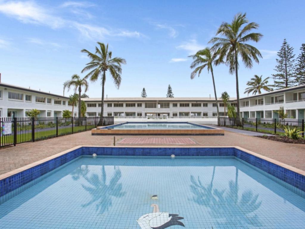 a swimming pool in front of a building with palm trees at Nalu - Hosted by Burleigh Letting in Gold Coast