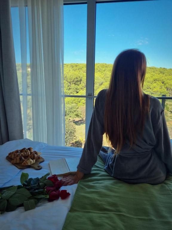 a woman sitting on a bed looking out of a window at Premantura Resort - Hotel & Restaurant in Premantura