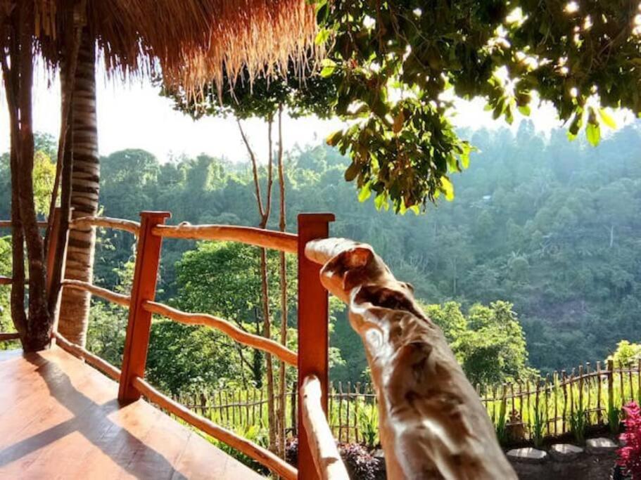 a dog sitting on a fence looking at the mountains at Dreamy Eco Tree House by 7 Waterfalls in Ambengan