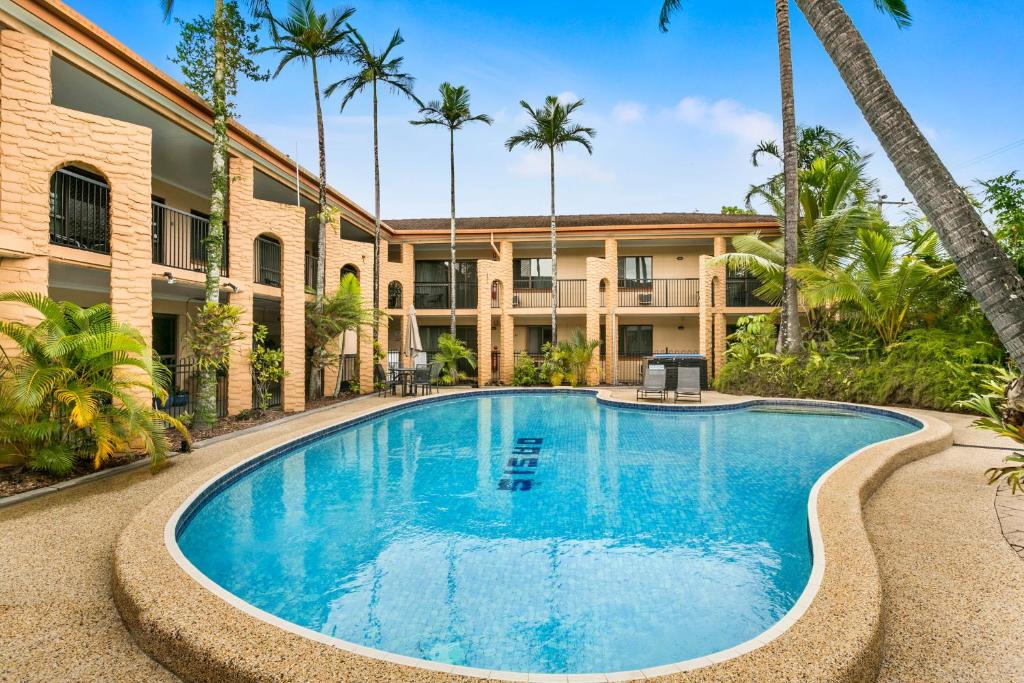 a swimming pool in front of a building with palm trees at Oasis Inn Apartments in Cairns