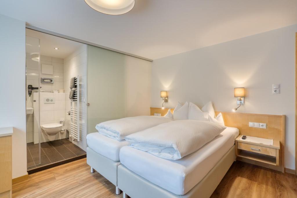 ein weißes Schlafzimmer mit einem großen Bett und einem Badezimmer in der Unterkunft Landhaus Maria in Stuben am Arlberg