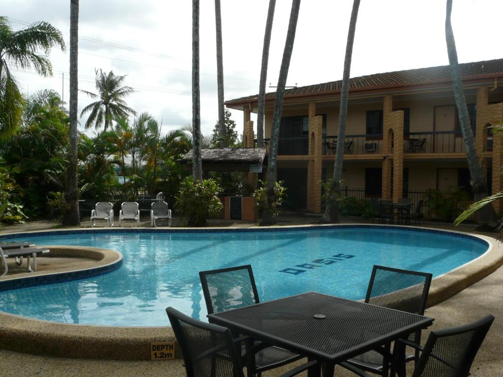 a pool with a table and chairs next to a building at Oasis Inn Apartments in Cairns