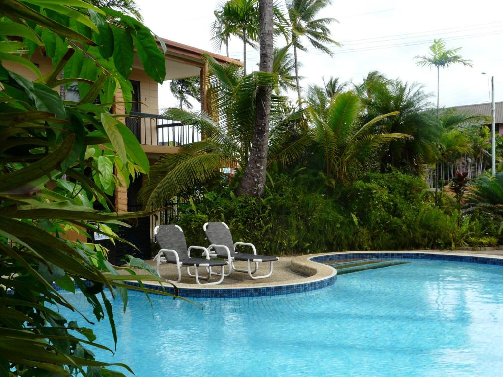 a swimming pool with lounge chairs and a house at Oasis Inn Apartments in Cairns