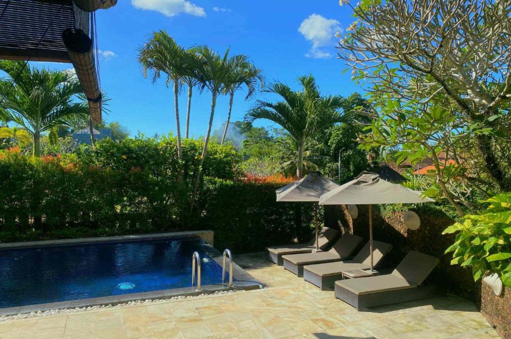 a swimming pool with two chairs and an umbrella at Karvaka Villa in Canggu