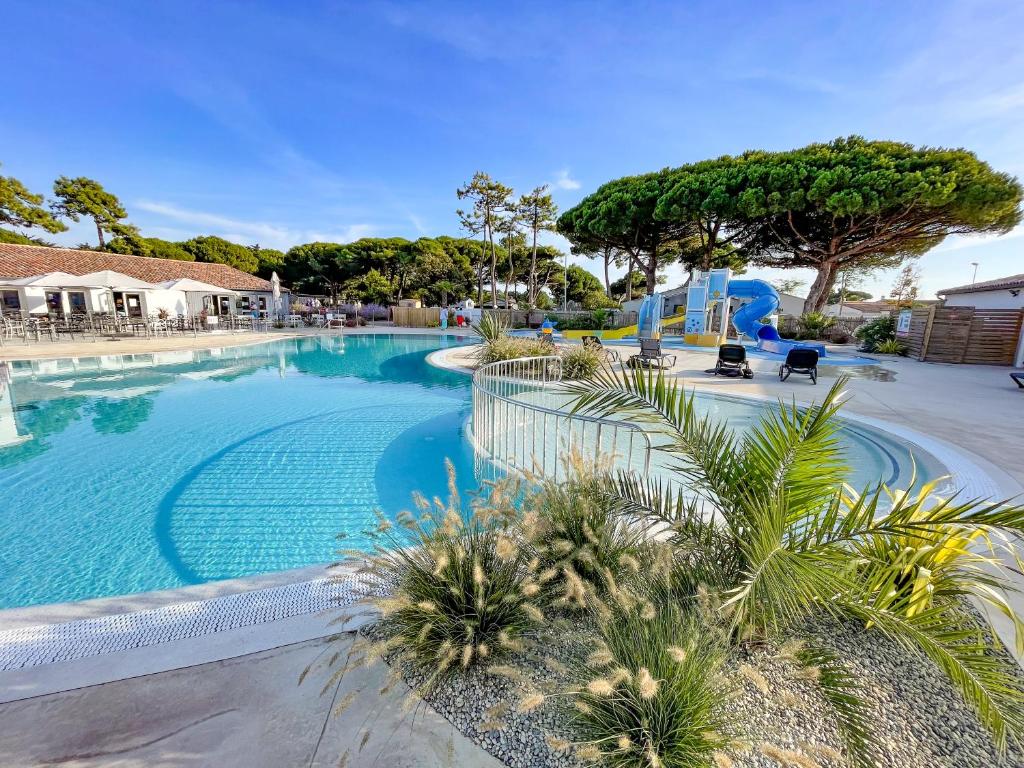 a large swimming pool with palm trees in a resort at Camping Le Suroit in Le Bois-Plage-en-Ré