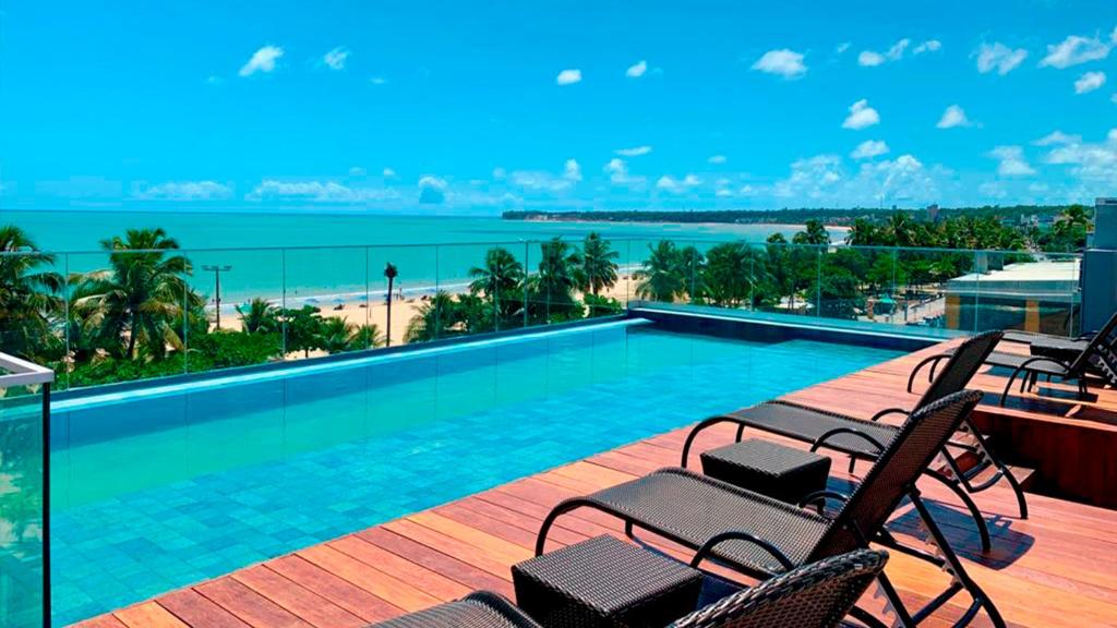 a swimming pool on a balcony with chairs and the ocean at Infinity at the Sea by Matka in João Pessoa