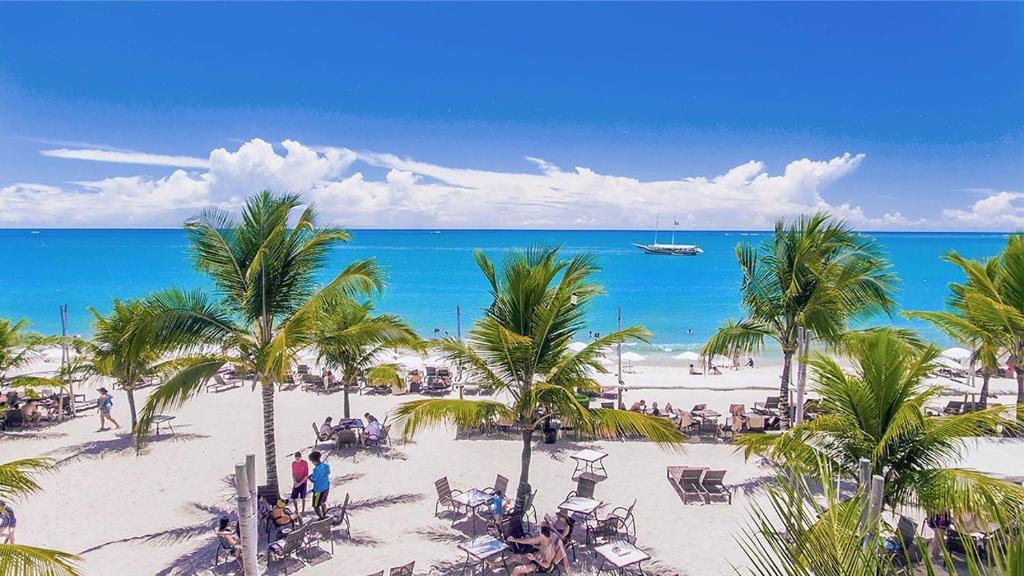 una playa con palmeras y un barco en el agua en Oásis do Mutá Residencial, en Porto Seguro