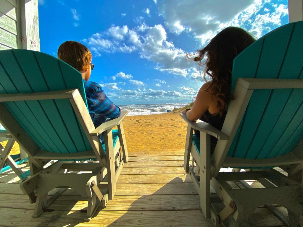 a boy and a girl sitting in chairs on the beach at John Yancey Oceanfront Inn in Kill Devil Hills