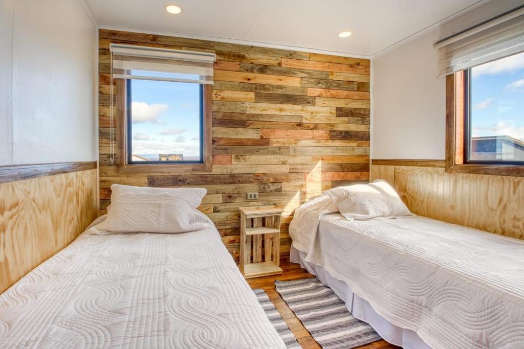 two beds in a room with wooden walls and windows at Cabañas Natales Rotundo in Puerto Natales
