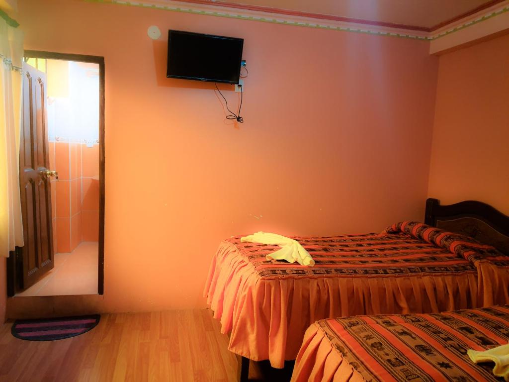 a bedroom with two beds and a television on the wall at HOSTAL Luz YHOBIMAR in Copacabana