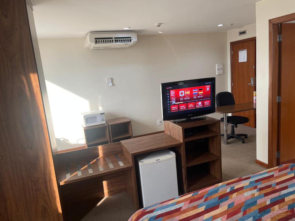 a room with a bed and a television and a desk at PROMOÇÃO EXECUTIVA COM BANHEIRA E FLATS SEM BANHEIRA- Melhor Hotel De Taguatinga in Taguatinga