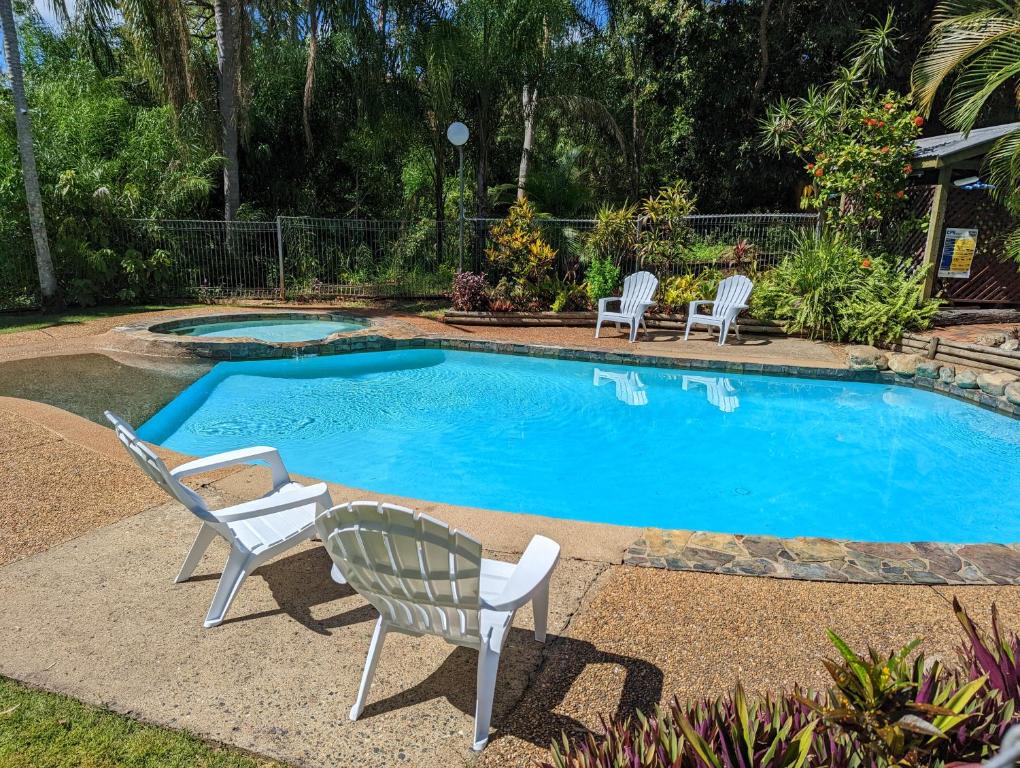 a swimming pool with two chairs and a chair next to it at Gumnut Glen Cabins in Yeppoon