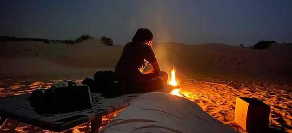 a person sitting next to a fire in the desert at Jodhpur Camel Safari & Overnight Stay In Desert Jodhpur NotOnMap in Jodhpur