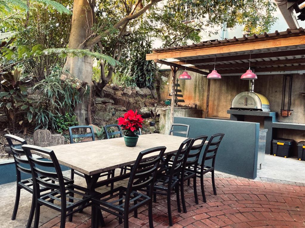 une table en bois avec des chaises et un pot de fleurs rouges dans l'établissement Ladybird, à Durban