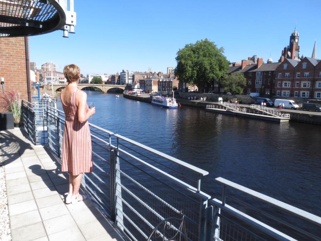 uma mulher de pé sobre um corrimão olhando para um rio em 3 Emperors Wharf with Stunning River Views em York