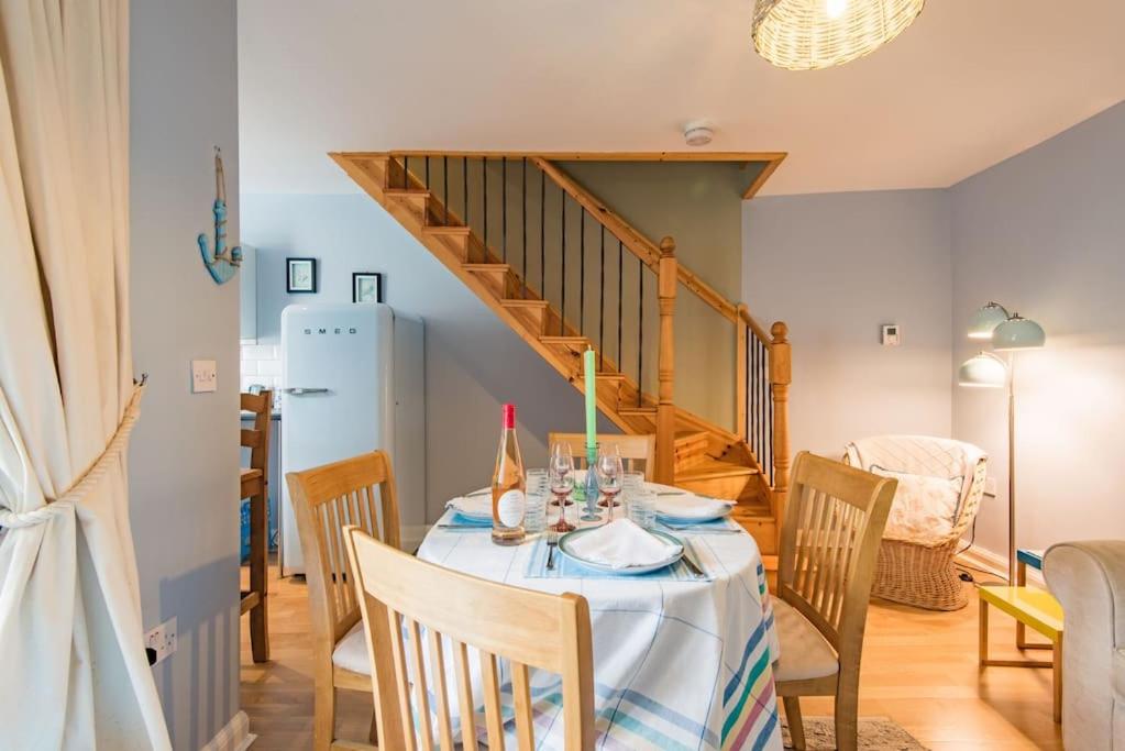 a dining room with a table and a staircase at Curious Cottage in Deal