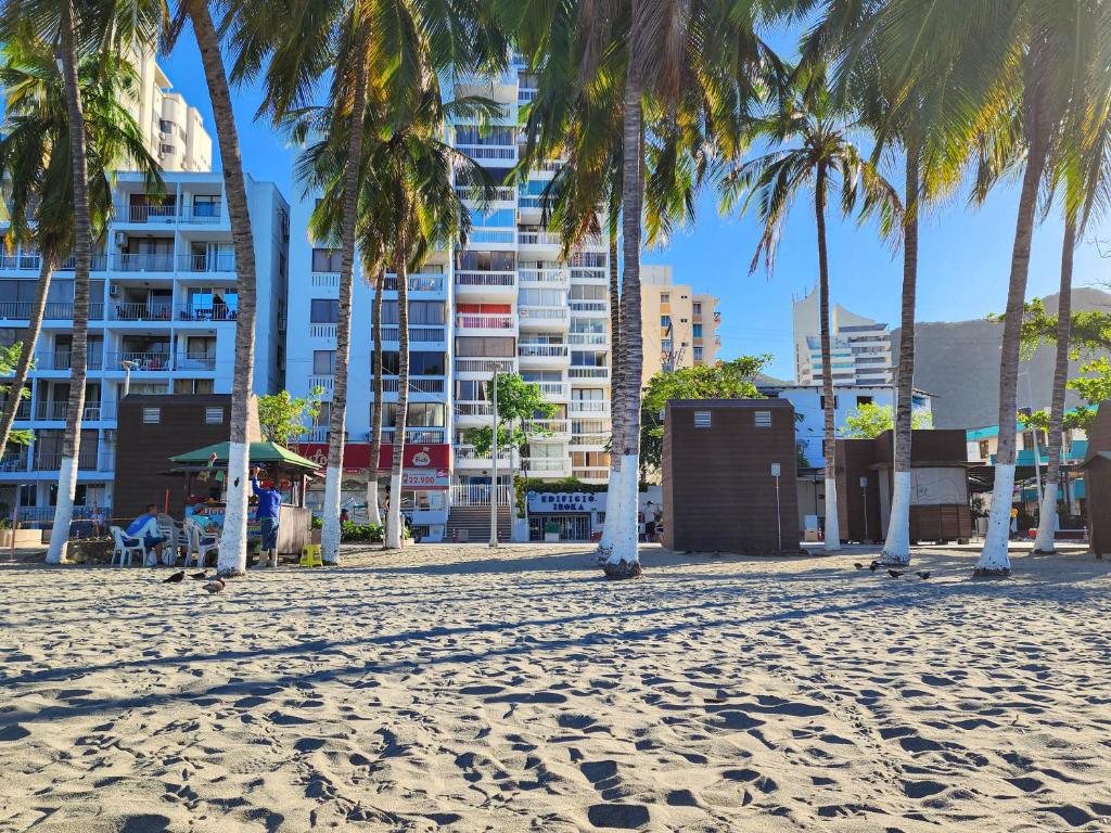 a beach with palm trees in front of a building at Apartamentos frente al mar IROKA -By Bedviajes in Santa Marta