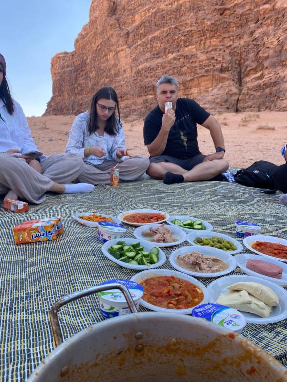 a group of people sitting on the beach eating food at wadi rum land mars in Wadi Rum