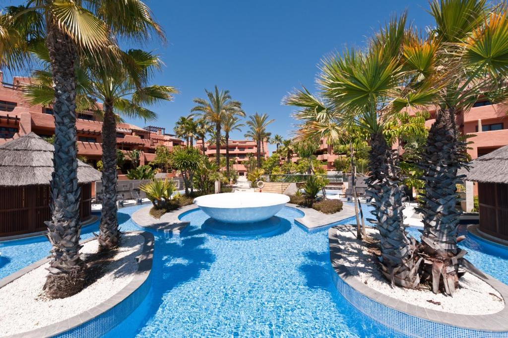 uma grande piscina com palmeiras e uma fonte em Mar Azul ApartHotel em Estepona