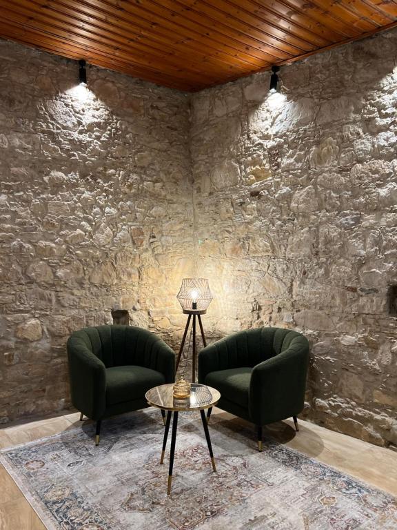2 grüne Stühle und ein Tisch in einem Zimmer mit einer Steinmauer in der Unterkunft VHouse at Vouni in Vouni