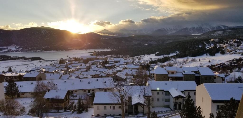 un pueblo cubierto de nieve con el sol en el fondo en Studio avec loggia Les Angles - Superbe vue sur Lac et Montagnes en Les Angles