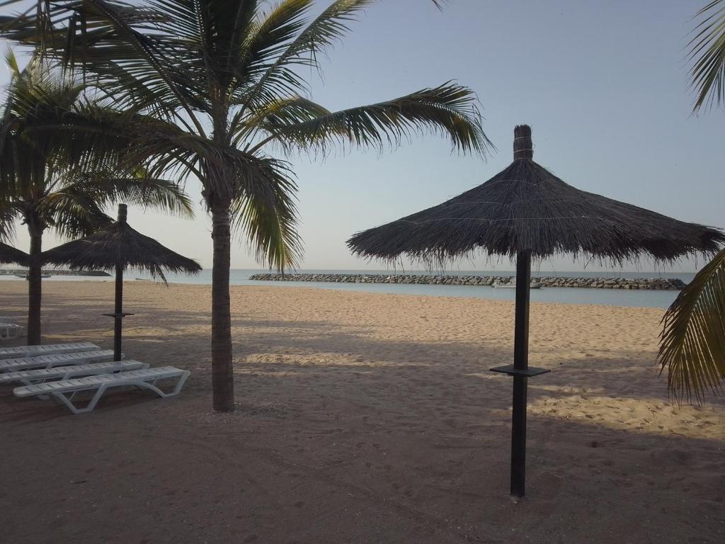 dos sombrillas y un banco en una playa en KEUR DIAM - Maison de la Paix en Saly Portudal