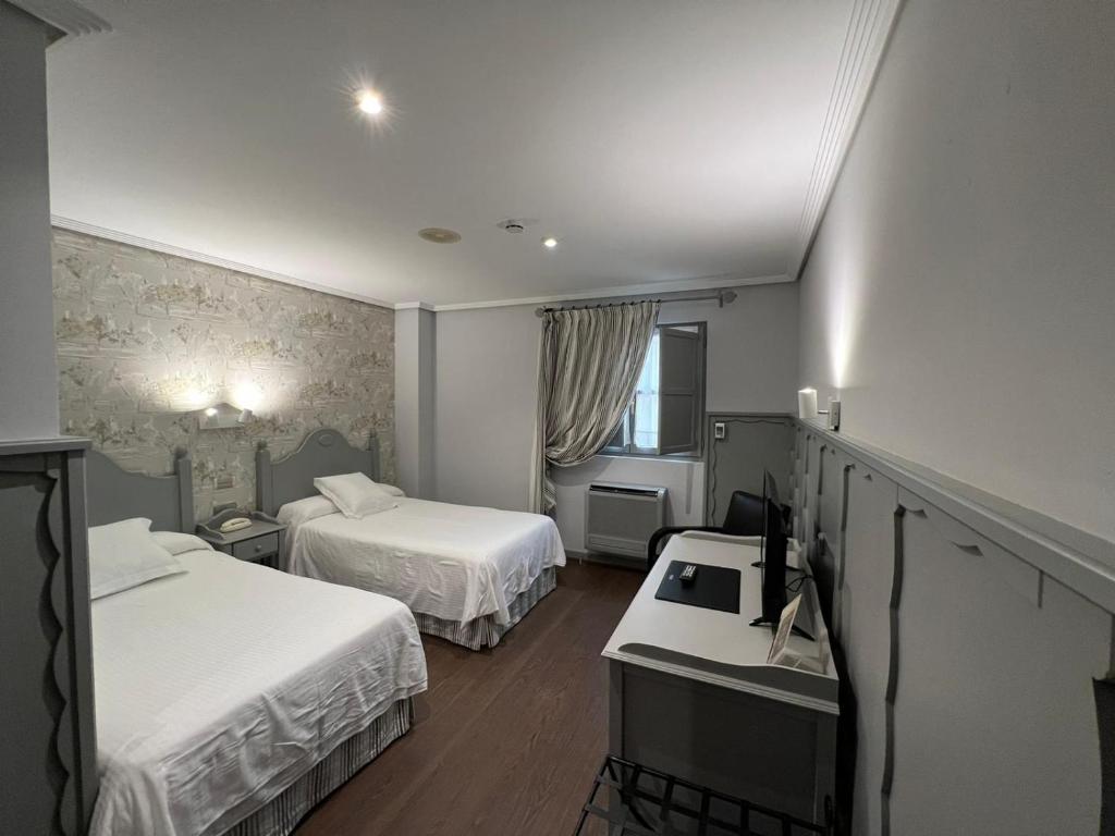 Una habitación de hotel con dos camas y un escritorio. en Hotel Comillas, en Comillas