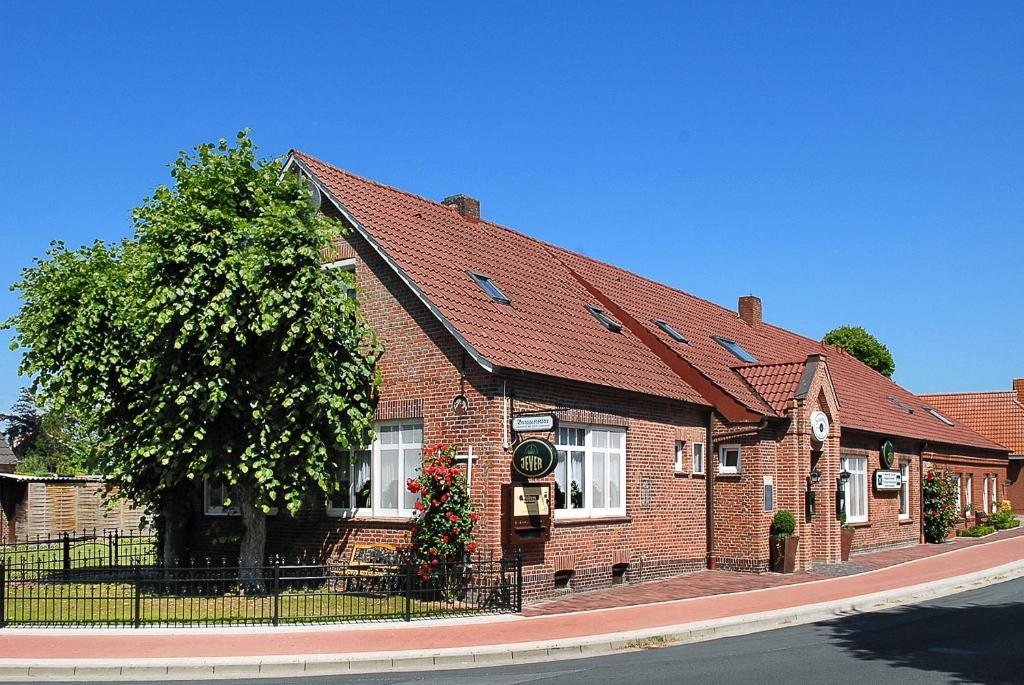 un bâtiment en briques avec un arbre devant lui dans l'établissement Pension Burggaststätte Heyken, à Neuharlingersiel