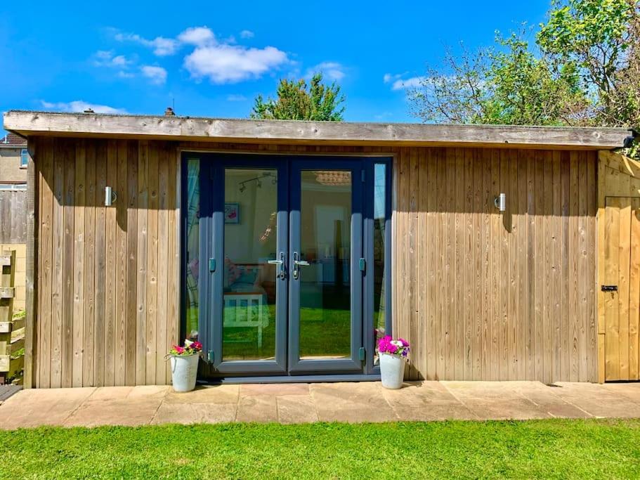 a wooden shed with glass doors and two plants at The Old Beauty Room in Paulton