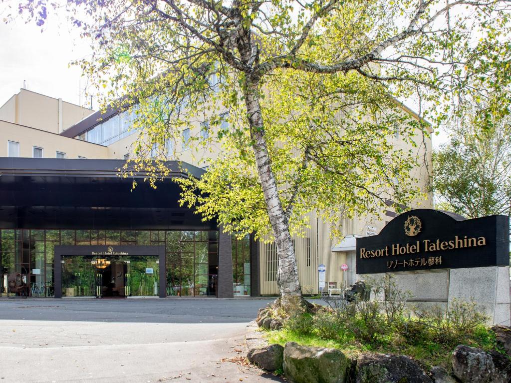 a sign in front of a building with a tree at Resort Hotel Tateshina in Chino